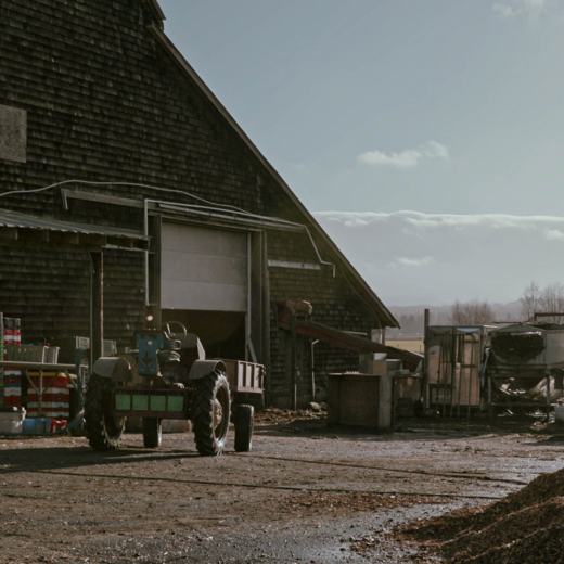 A tractor is parked outside of an old, brown barn.